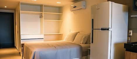 Un dormitorio con una cama, un armario blanco y un refrigerador blanco.