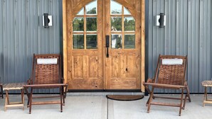 A wooden double door with glass panels, flanked by two wicker chairs with cushions.