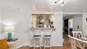A compact living space with a kitchenette, two bar stools, a dining table, and a sofa. - Robinhood Beach Villa (Sarasota)