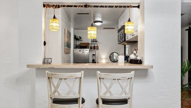 A kitchen with a wooden countertop, two white chairs, and hanging pendant lights. - Robinhood Beach Villa (Sarasota)