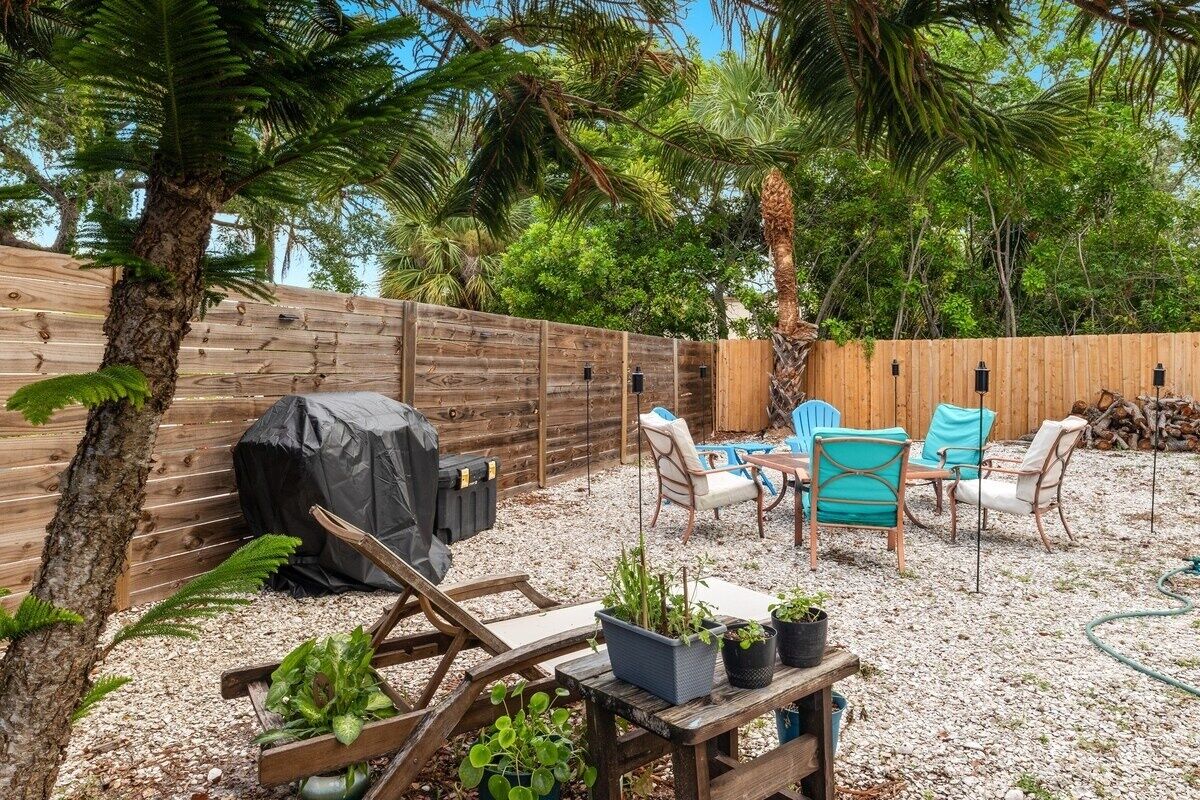 Een achtertuin met houten schutting, tuinmeubilair en planten in potten.