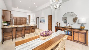A modern kitchen with a bar area, wooden cabinets, and a dining table with a centerpiece. - Quivira PH 3BR Premium Condo w/ Golf Cart (Cabo San Lucas)