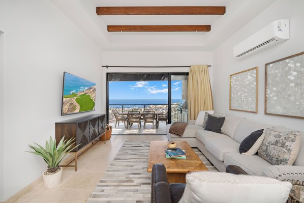 A modern living room with a sofa, coffee table, and a view of the ocean through large windows.