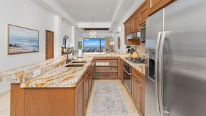 A spacious kitchen with a large island, wooden cabinets, stainless steel appliances, and a view to the outside. - Quivira PH 3BR Premium Condo w/ Golf Cart (Cabo San Lucas)
