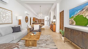 A spacious living room with a sofa, coffee table, and a large painting of a golf course. - Quivira PH 3BR Premium Condo w/ Golf Cart (Cabo San Lucas)