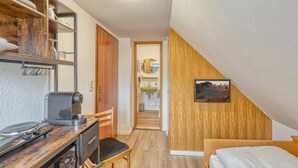 A compact bedroom with a wooden desk, chair, and a bed. A bathroom with a sink and mirror is visible through an open door. - Nice apartment in Bischofsheim (Bischofsheim)