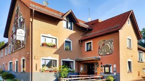A two-story building with a traditional architectural style, featuring a balcony with railings, multiple windows with flower boxes, and a prominent coat of arms on the facade. - Nice apartment in Bischofsheim (Bischofsheim)