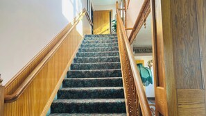 A wooden staircase with carpeted steps leading to a room with a large painting. - Victorian Inn Motel & Suites (Superior)
