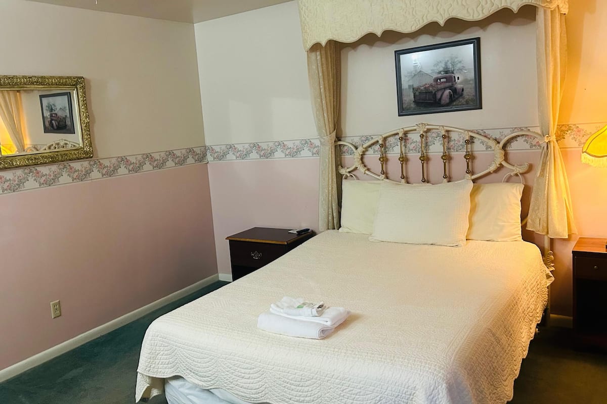 A neatly made bed with a white quilt, a bedside table with a lamp, and a framed picture on the wall.