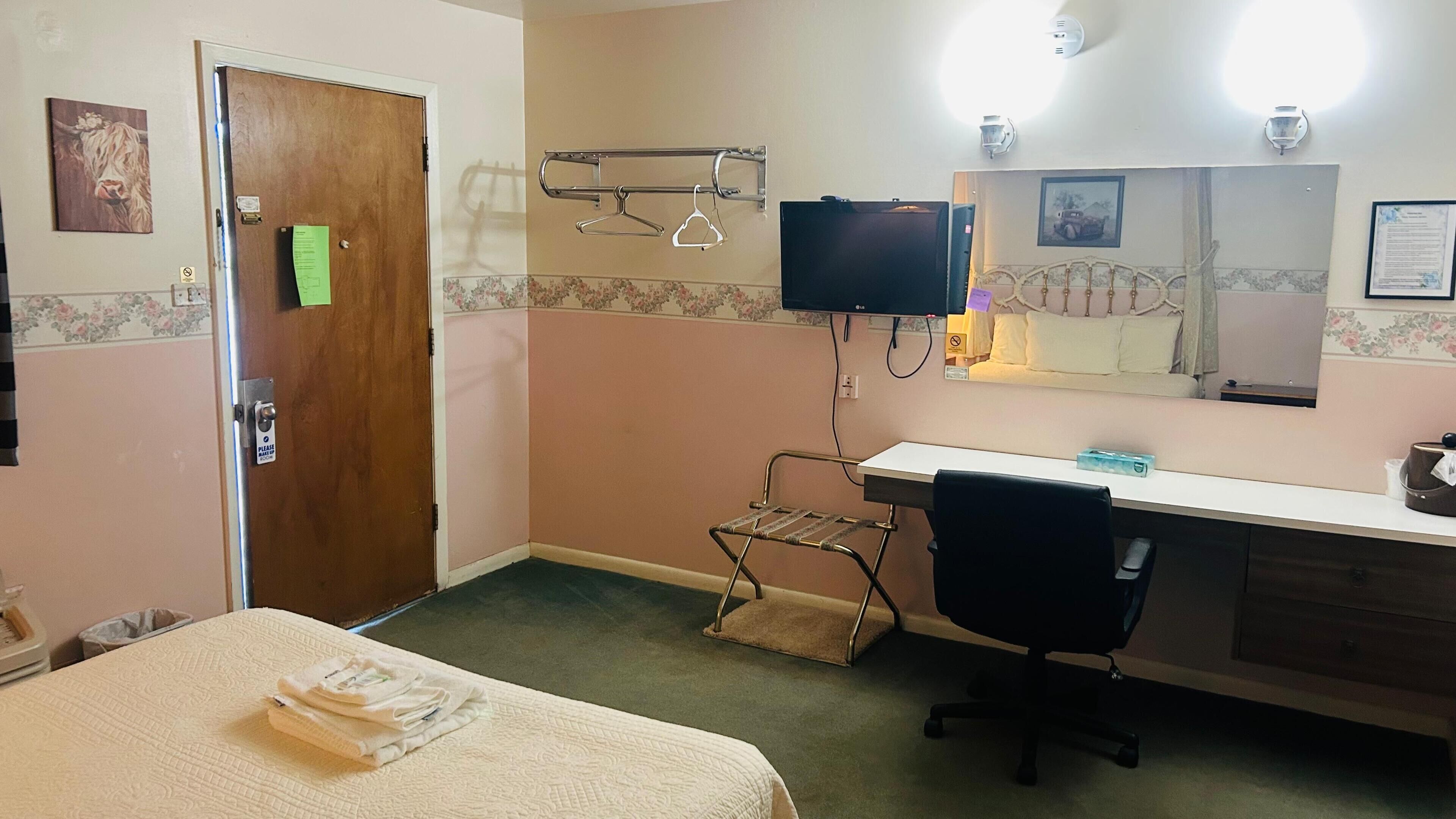 A hotel room with a bed, a desk, a chair, a TV, and a mirror.