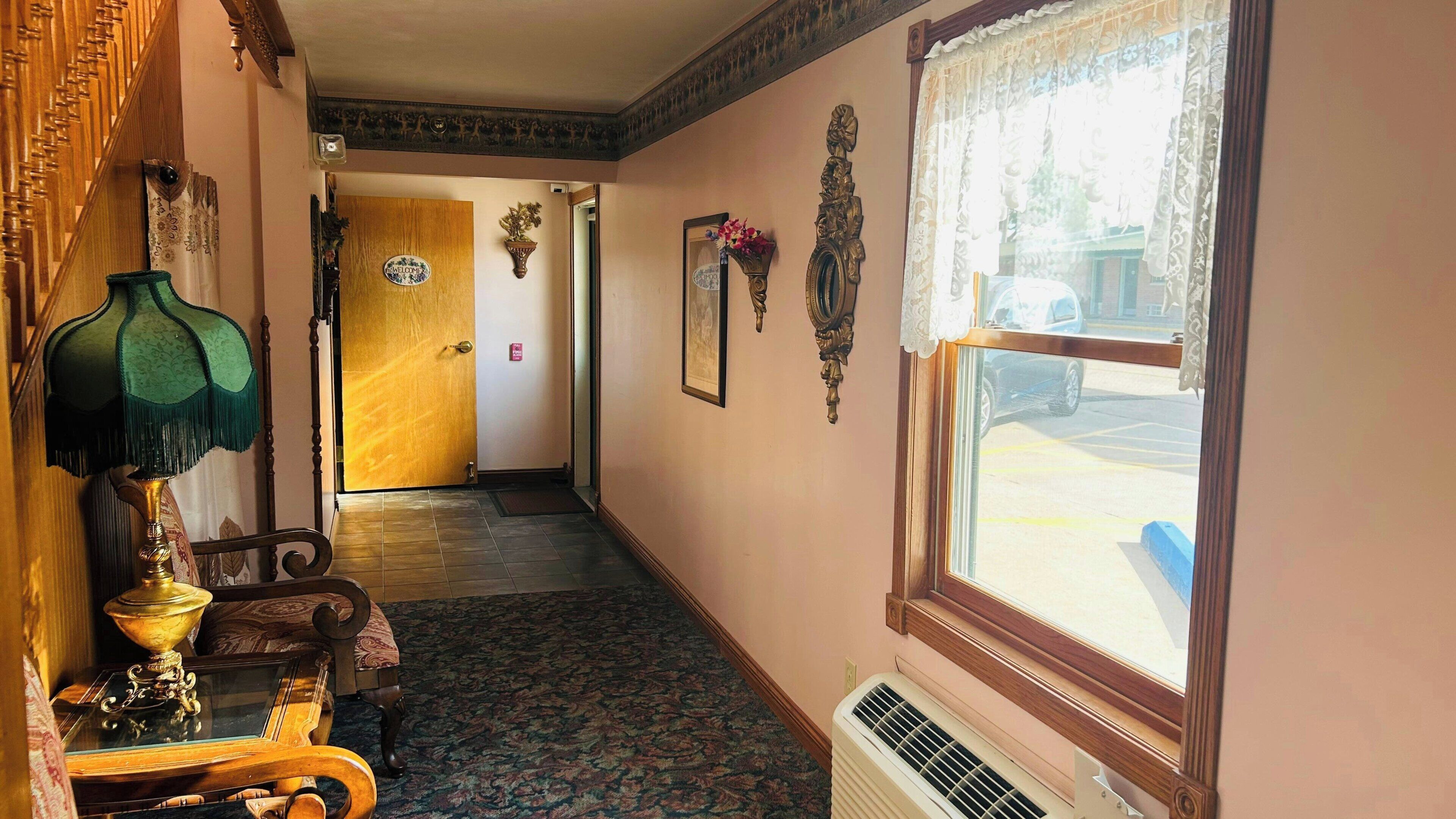 A hallway with a wooden door, a 'Welcome' sign, a mirror, and a window with a view of the street.