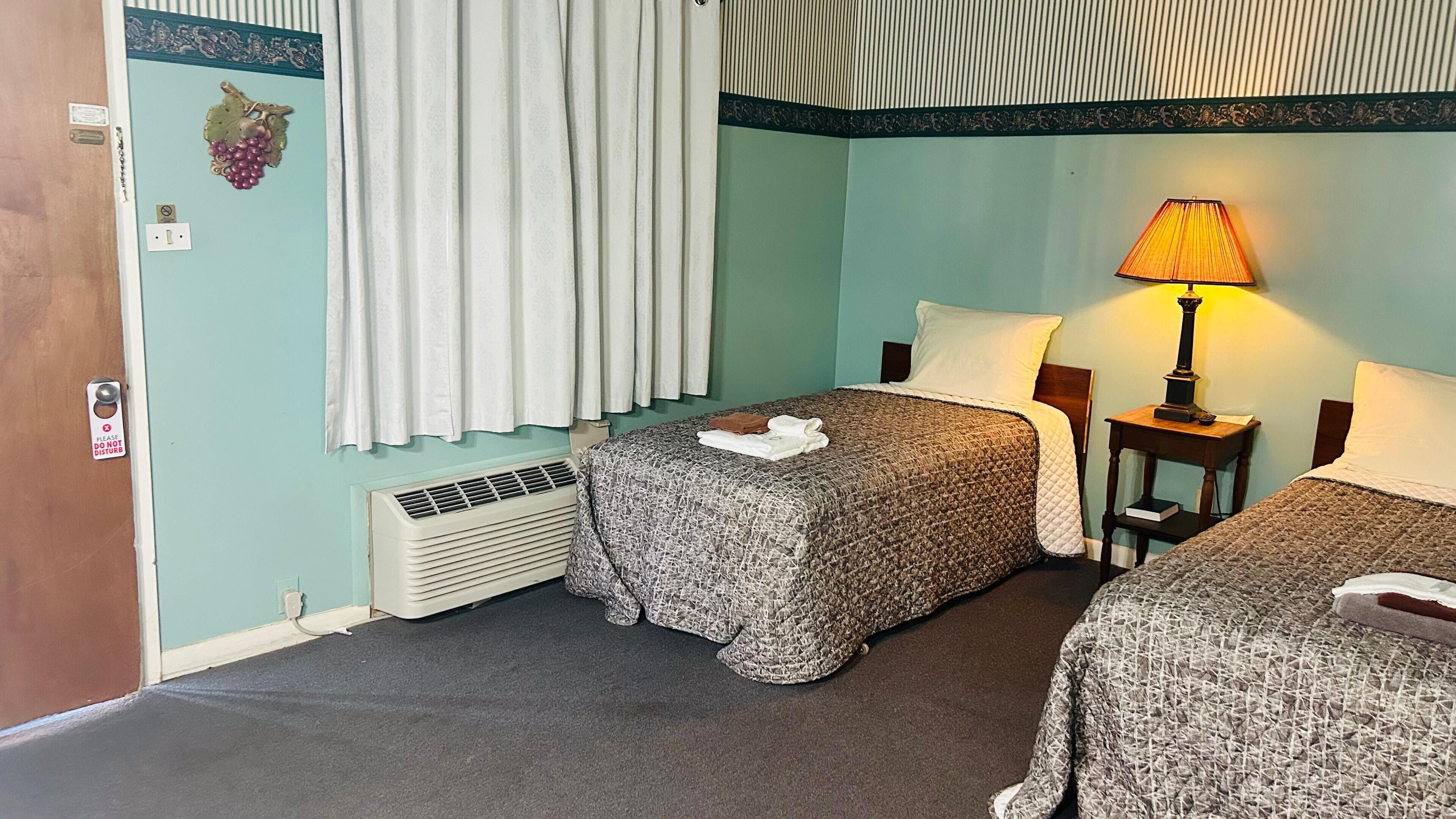 A hotel room with two beds, a heater, a lamp, and a decorative grape on the wall.