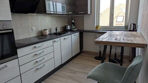 Una cucina moderna con mobili chiari in legno, una cappa aspirante nera, forno a incasso e una finestra con vista sugli edifici.