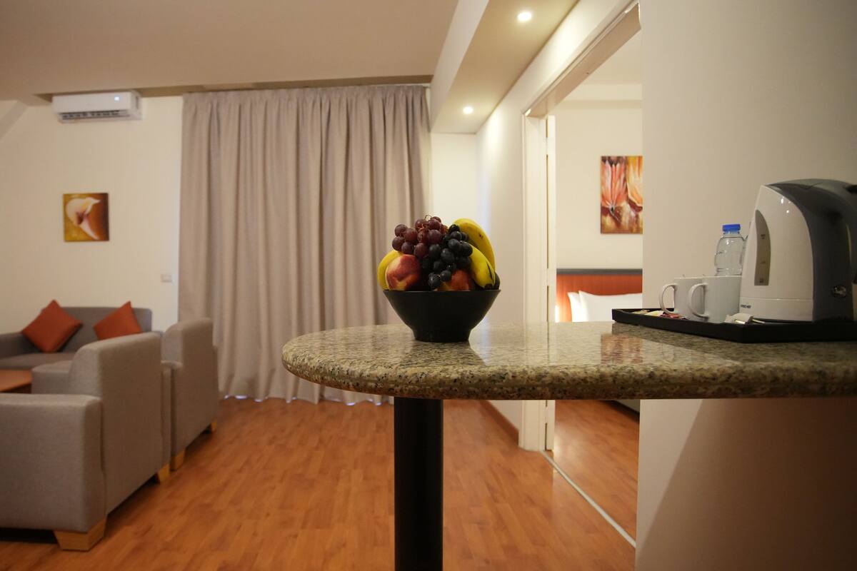 Una habitación de hotel moderna con una mesa redonda de granito, un sofá gris y una cafetera.