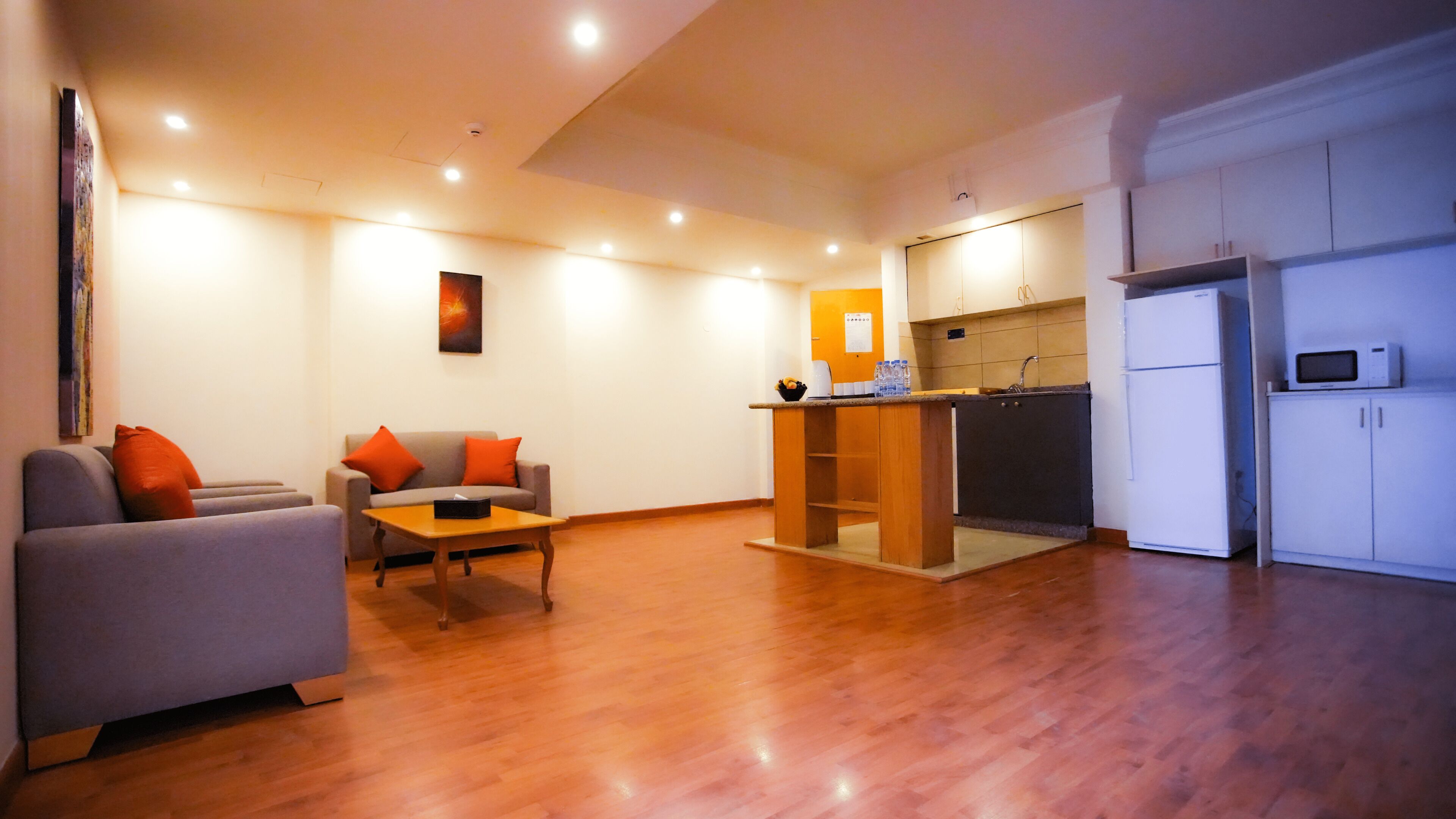 A modern living room with a sofa, a coffee table, and a kitchen area with a refrigerator and microwave.