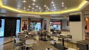 A modern dining area with tables and chairs, a flat-screen TV on the wall, and a ceiling with recessed lighting. - Manara Riva Suites  (Beirut)