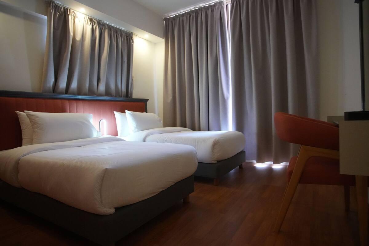 Habitación de hotel con dos camas, suelo de madera y un escritorio con una silla.