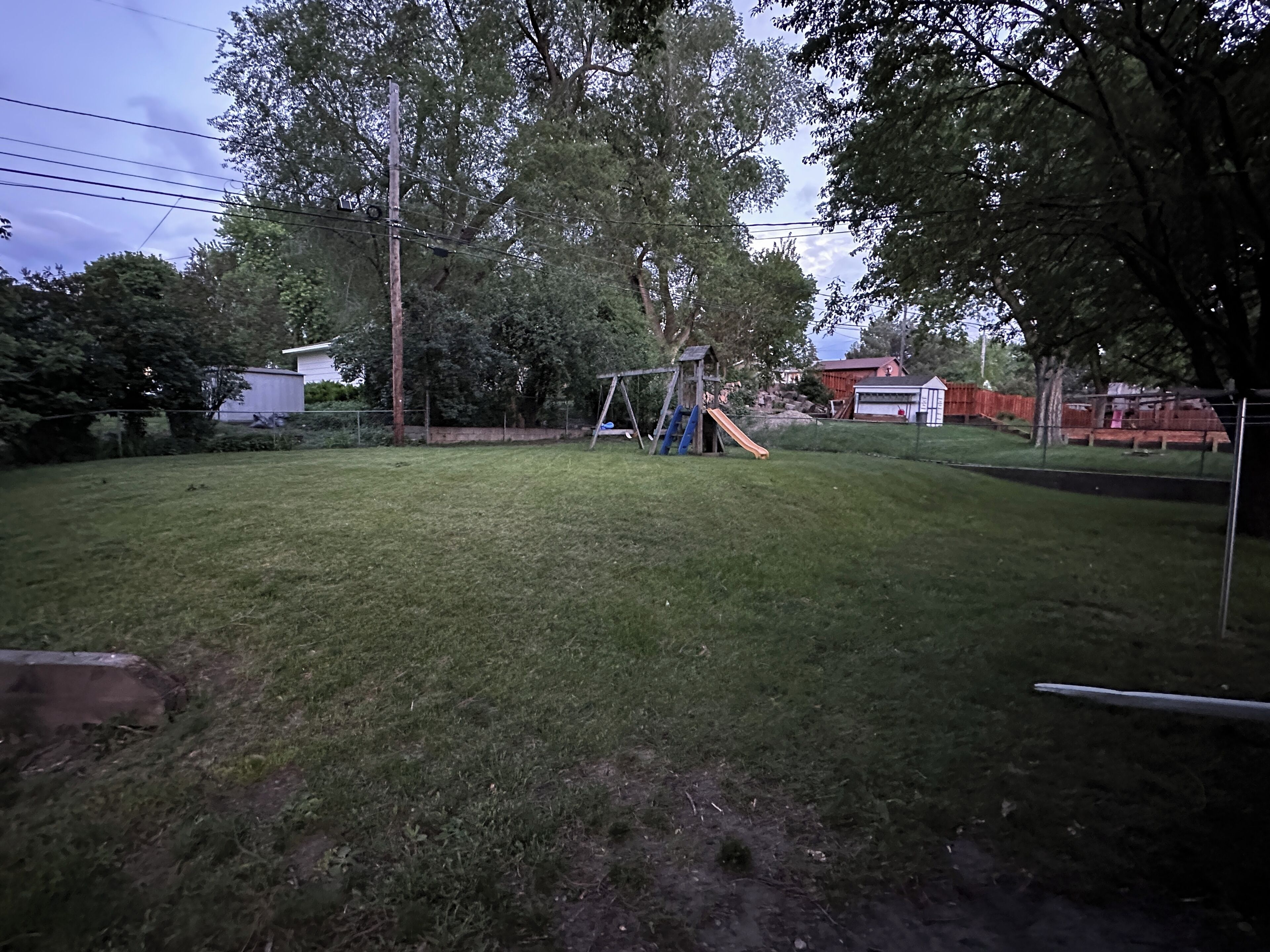 Un jardin avec une balançoire, un toboggan et une zone délimitée par une clôture.