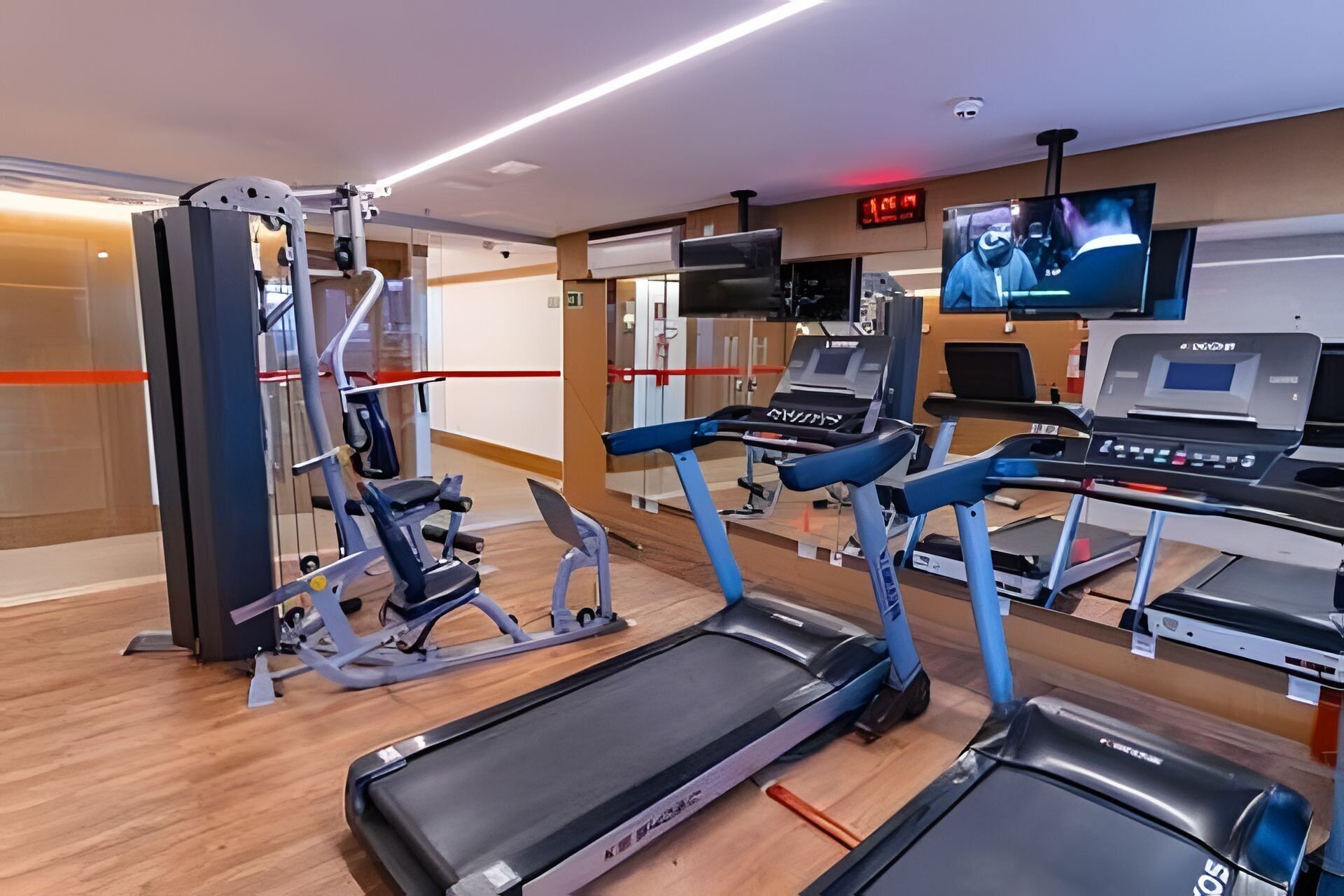 Un gimnàs amb cintes de córrer, aparells de musculació i una pantalla de televisió.