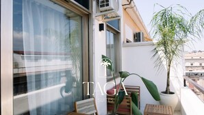 A balcony with a wooden table and chairs, a potted plant, and an air conditioning unit. - Taga suites  (Catania)