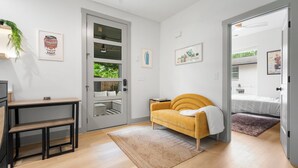 Ein modernes Wohnzimmer mit einer Couch, einer Bank, einem kleinen Tisch und einer Tür zu einem anderen Raum.