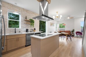 Uma cozinha moderna com uma ilha central, eletrodomésticos embutidos e uma área de jantar com mesa e cadeiras de madeira.