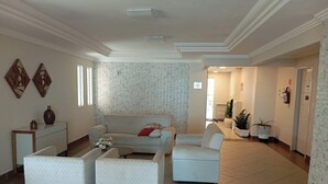 A spacious living room with a white sofa, two armchairs, and a coffee table. There is a brick-patterned wall behind the sofa and a tiled floor.