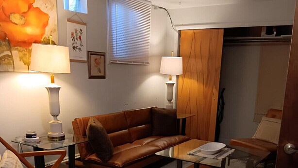 A cozy living room with a brown leather sofa, a glass coffee table, a wooden rocking chair, and a patterned rug. - Charming 1-Bedroom  Apartment in Great Neighborhood (Great Falls)