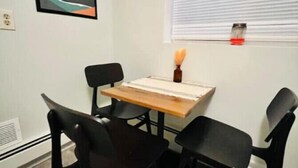 A small dining area with a wooden table and four black chairs. There is a painting on the wall and a window with blinds. - Charming 1-Bedroom  Apartment in Great Neighborhood (Great Falls)