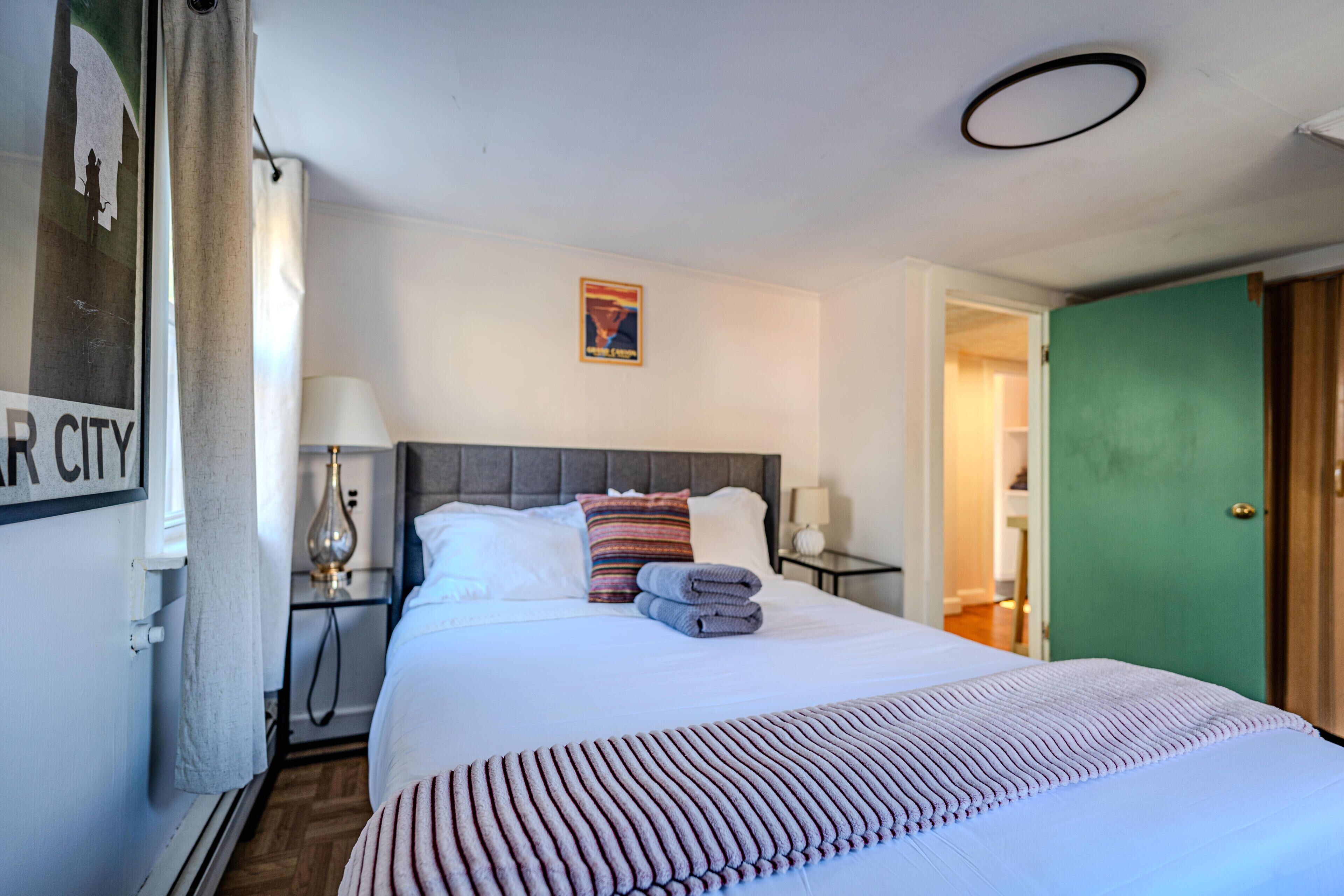 A hotel room with a neatly made bed, a headboard, a nightstand with a lamp, and a green door.
