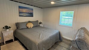 A bedroom with a bed, a nightstand, a window, and a painting on the wall.