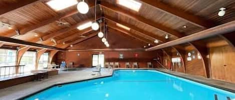 An indoor swimming pool with wooden architecture, a lifeguard chair, and a pool ladder.
