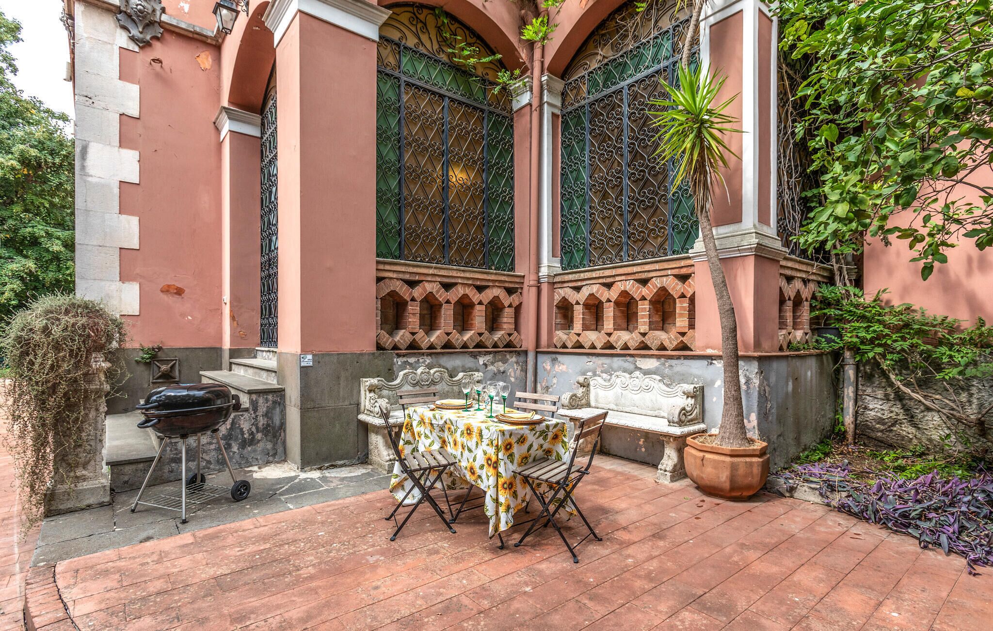 An outdoor patio with a table set for dining, surrounded by a brick wall with decorative iron gates and a potted plant.