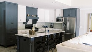 A modern kitchen with dark cabinetry, a central island with bar stools, and stainless steel appliances. - Spacious, Private, Beautiful Lot in Holiday Shores (Dadeville)