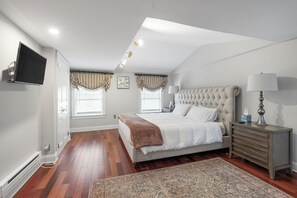 A bedroom with a large bed, a bedside table, a TV mounted on the wall, and a window with curtains. - Spacious 6BR En Suite Rittenhouse Home! Sleeps 14! (Philadelphia)