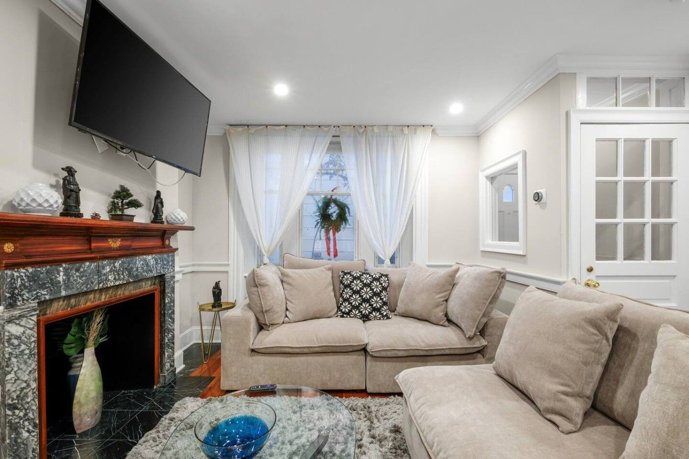 A living room with a fireplace, a television mounted on the wall, a sofa, and a window with curtains.