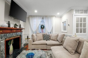 A living room with a fireplace, a sofa, a television, and a window with curtains. - Spacious 6BR En Suite Rittenhouse Home! Sleeps 14! (Philadelphia)