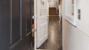 Un pasillo con una puerta negra identificada con el número '203', paredes blancas y un piso de mármol que conduce a una escalera.