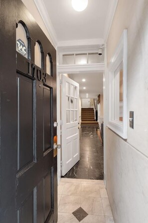 A hallway with a black door labeled '203', white walls, and a marble floor leading to a staircase. - Spacious 6BR En Suite Rittenhouse Home (Philadelphia)