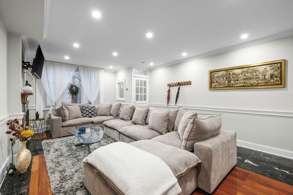 A modern living room with a beige sectional sofa, a glass coffee table, and a white throw blanket. - Spacious 6BR En Suite Rittenhouse Home! Sleeps 14! (Philadelphia)