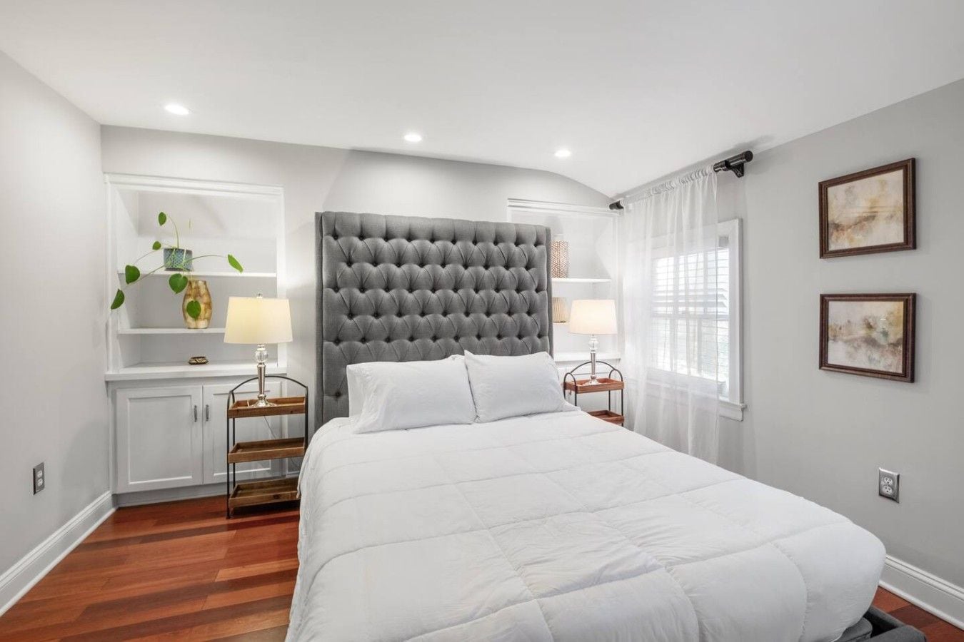 A bedroom with a large bed, a tufted headboard, bedside tables with lamps, a wardrobe, and artwork on the walls.