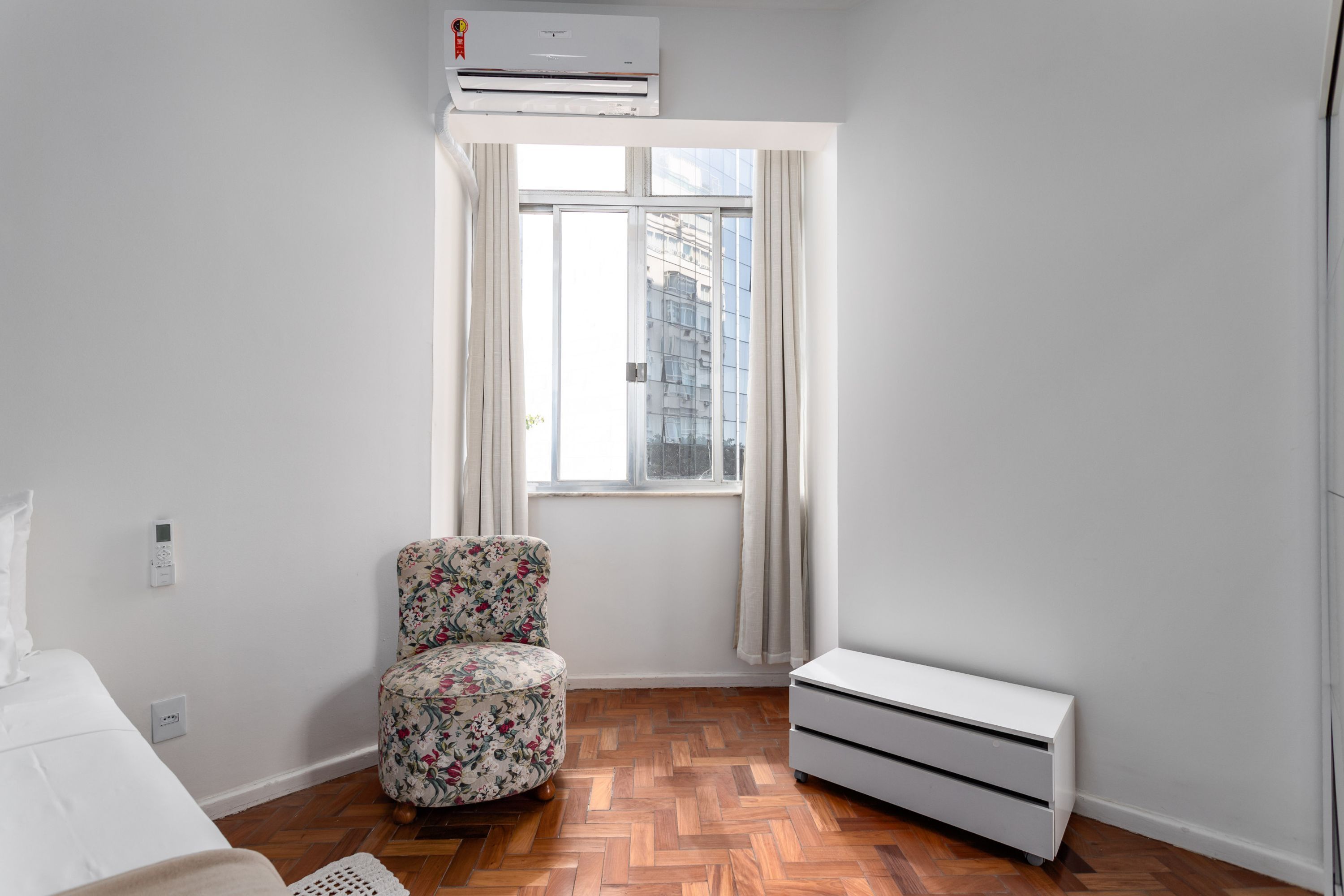 Ein Schlafzimmer mit einem Bett, einem Sessel, einem Heizgerät und einem Fenster mit Vorhängen.