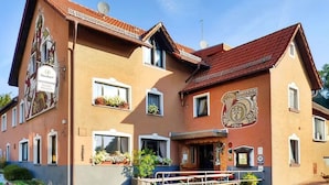 A two-story building with a traditional architectural style, featuring a balcony with railings, multiple windows with flower boxes, and a prominent coat of arms on the facade.