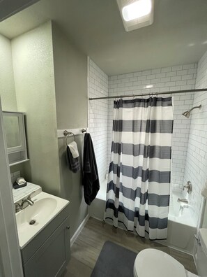 Ein Badezimmer mit einem weißen Waschbecken, einem Spiegel, einem Handtuchhalter mit Handtüchern, einem gestreiften Duschvorhang und einer Badewanne.