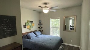 Un dormitorio con cama, ventilador de techo, ventana, cómoda y una cita motivacional en la pared.