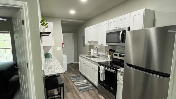 Una cocina moderna con armarios blancos, electrodomésticos de acero inoxidable y suelo de madera.