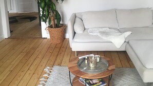 Ein Wohnzimmer mit einem weißen Sofa, einem Couchtisch mit Zeitschriften, einer Topfpflanze und Holzboden.