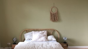 Ein Schlafzimmer mit einem Bett, Nachttischen, einer Hängelampe, einer Wanddekoration aus Makramee und einer Holzbank.