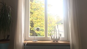 Ein Fenster mit weißen Vorhängen, ein Blumentopf, eine Schreibtischlampe und ein Kandelaber.