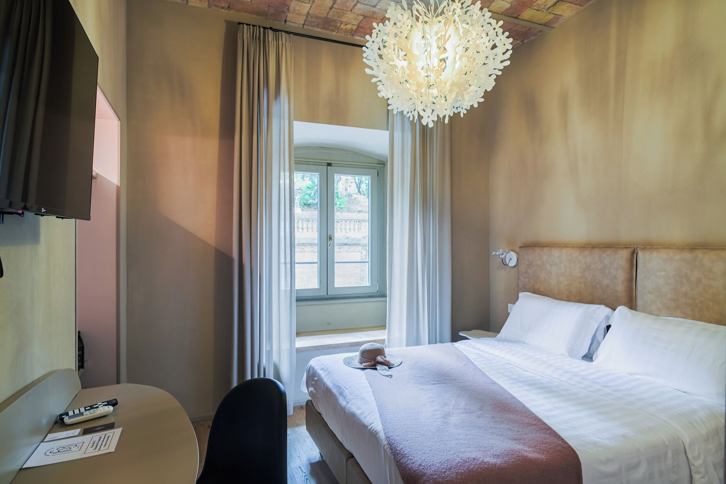 A hotel room with a bed, a desk, a chair, a television, and a window with curtains.